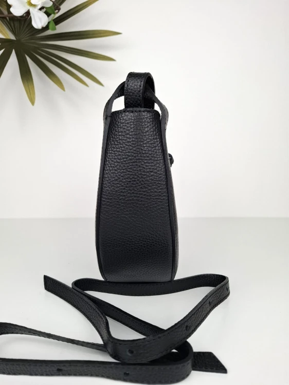 Czarna włoska torebka skórzana w kształcie łódeczki z regulowanym paskiem i złotymi okuciami na tle białej powierzchni i kwiatów